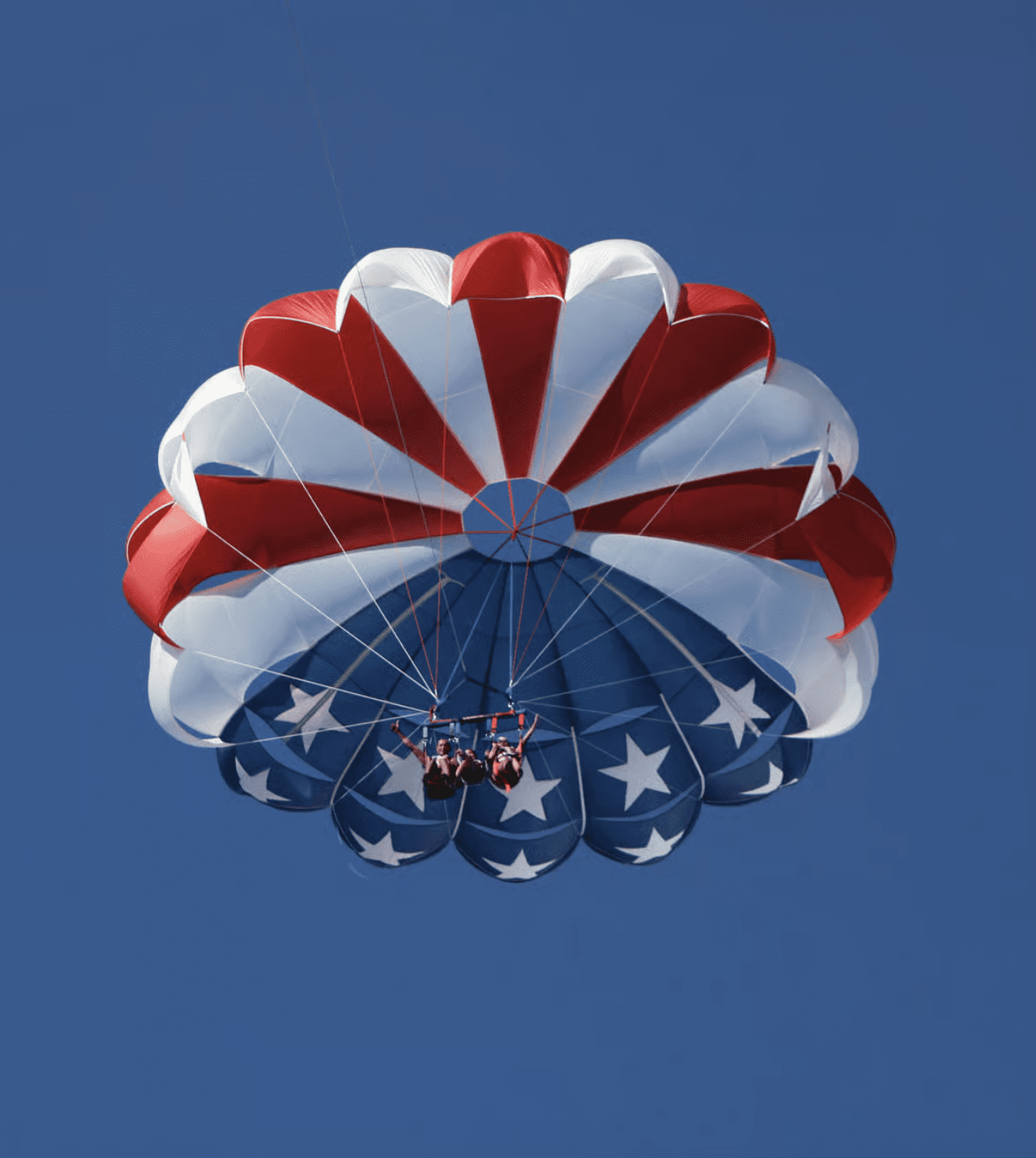 Parasailers flying beneath a patriotic parachute over Clearwater Beach