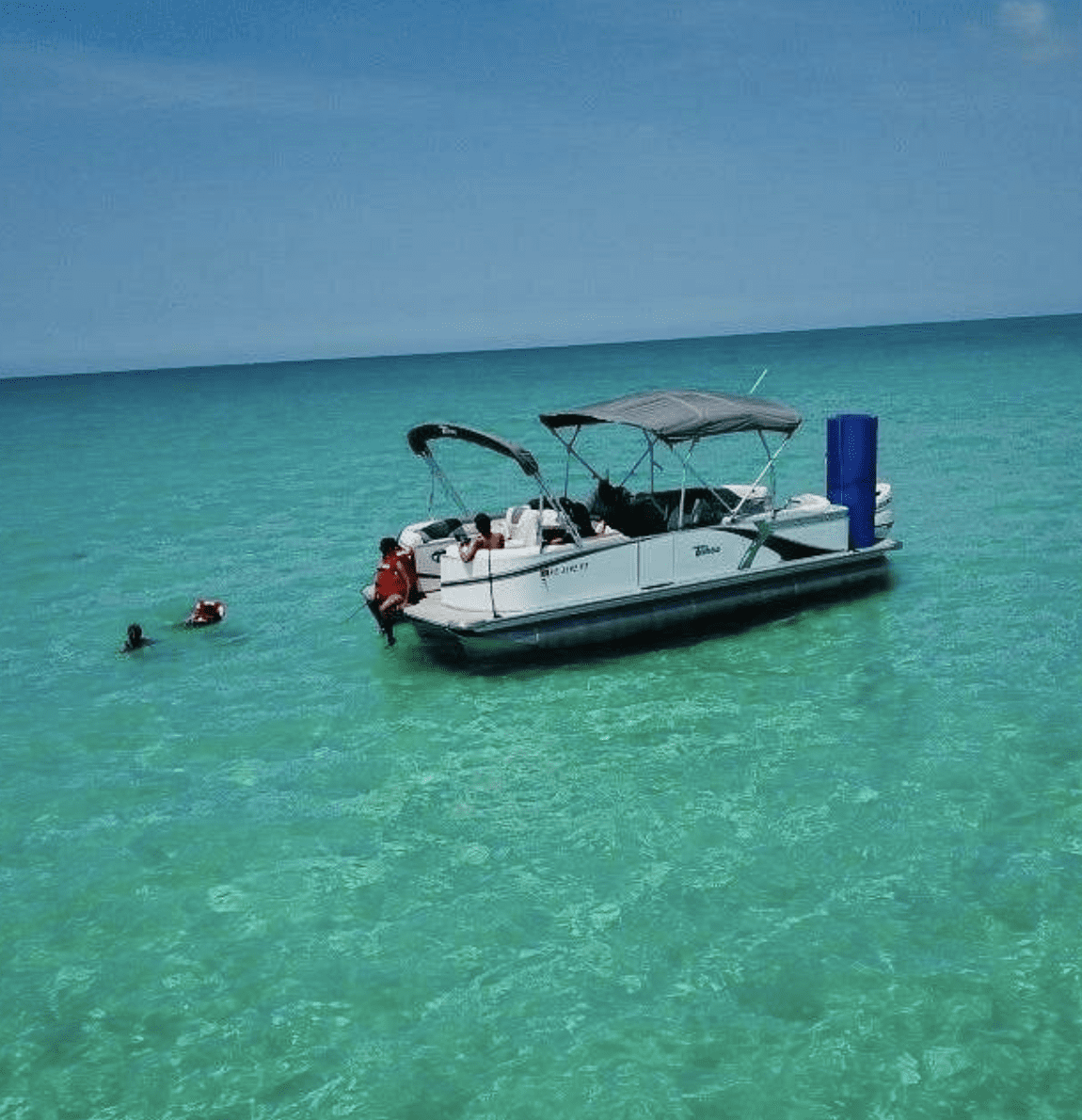 Pontoon boat anchored at a turquoise Clearwater Beach sandbar with people swimming nearby.