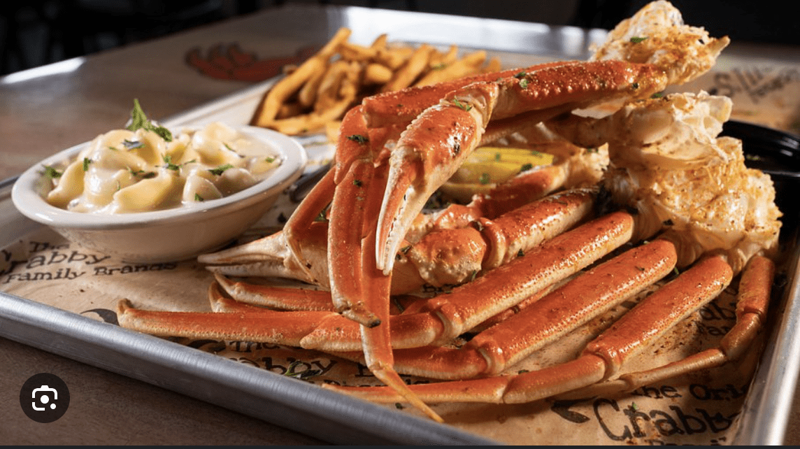 A tray of crab legs served with pasta, corn, and seasoned butter.