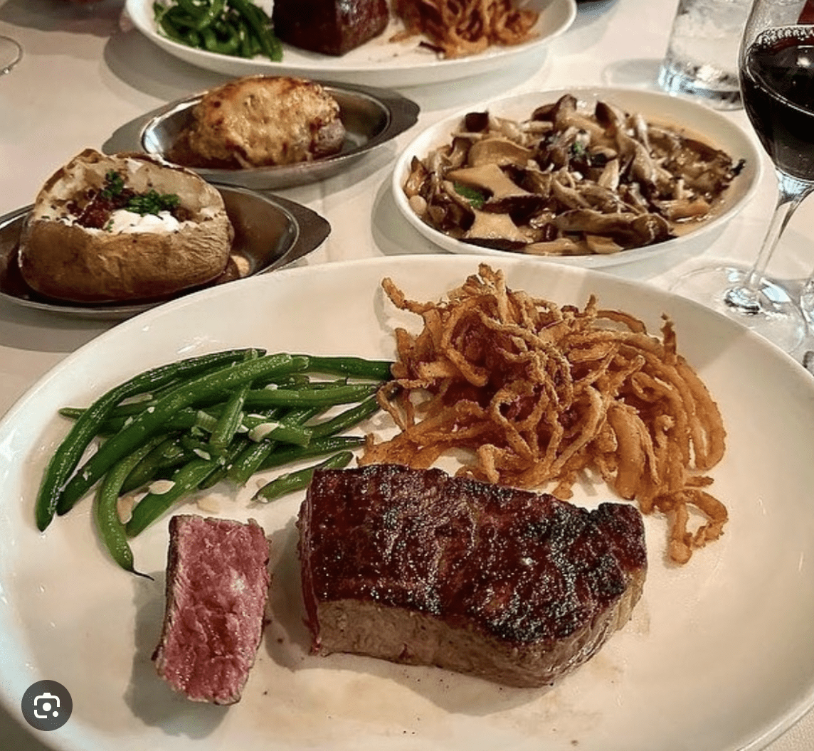 A plate with a grilled steak, crispy onion straws, and green beans, surrounded by additional side dishes.