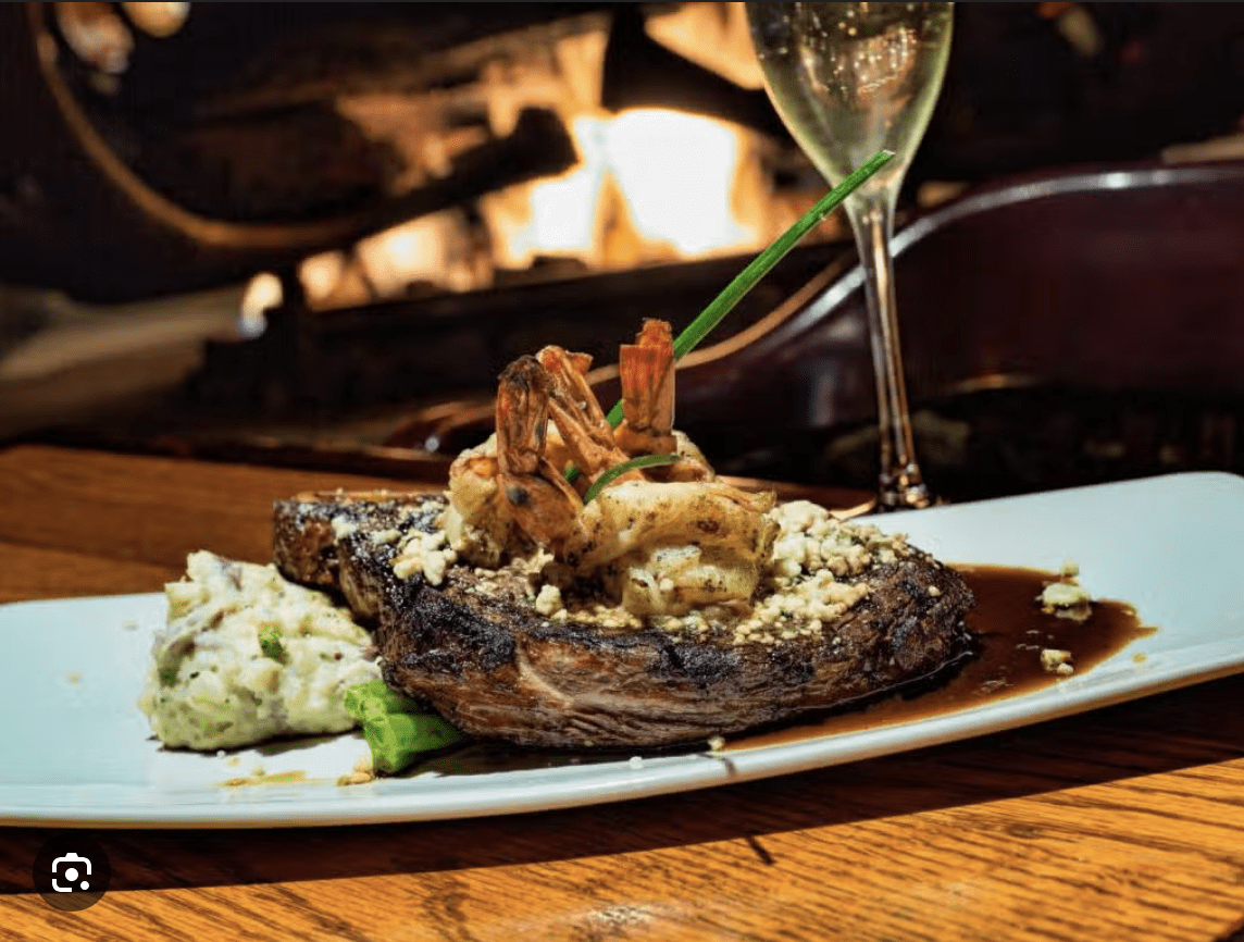 A grilled steak topped with shrimp and served with mashed potatoes on a white plate.
