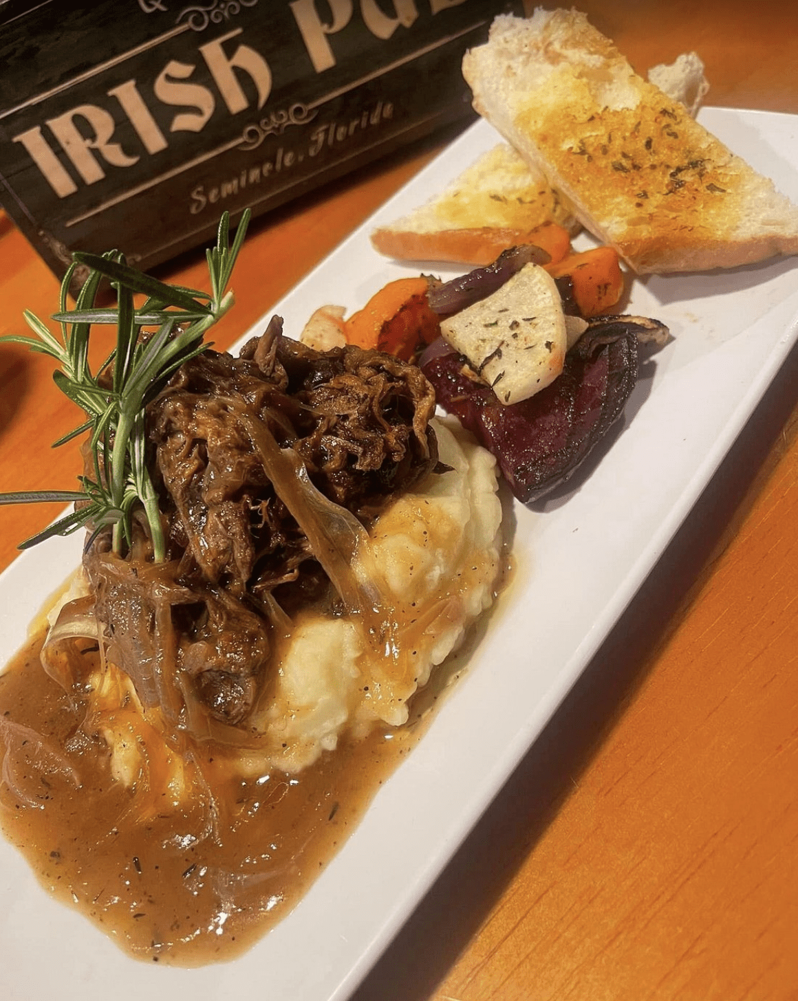 Braised beef served on mashed potatoes with gravy and roasted vegetables.