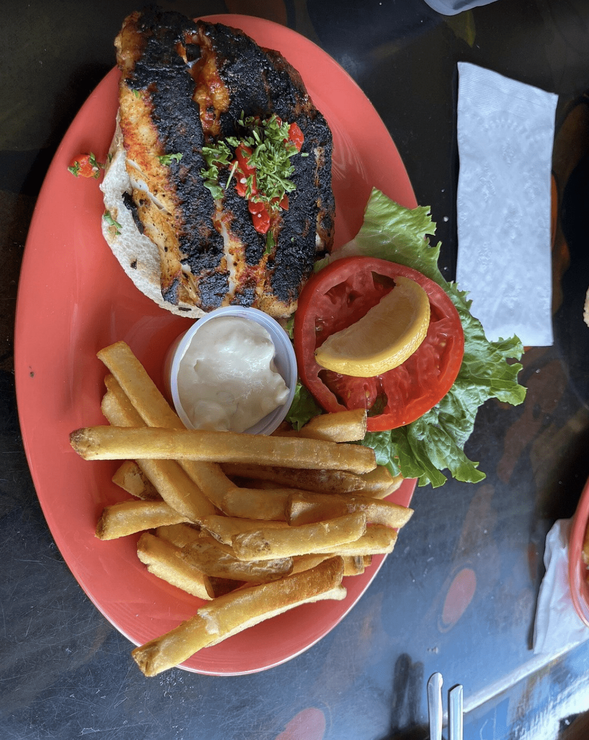 A grilled chicken sandwich served with lettuce, tomato, fries, and a side of dipping sauce.
