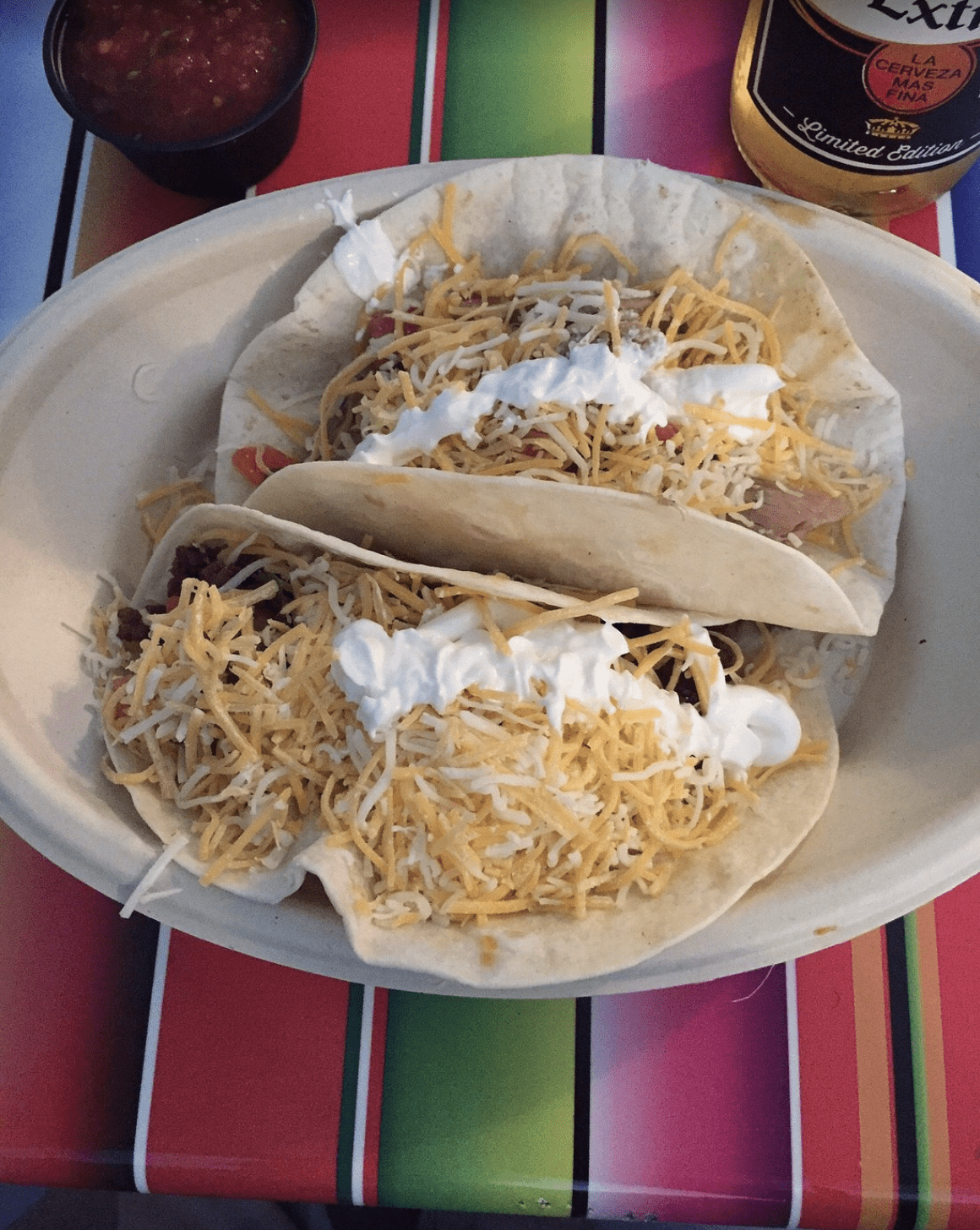 Two soft flour tacos filled with seasoned beef, shredded cheese, tomatoes, and sour cream.