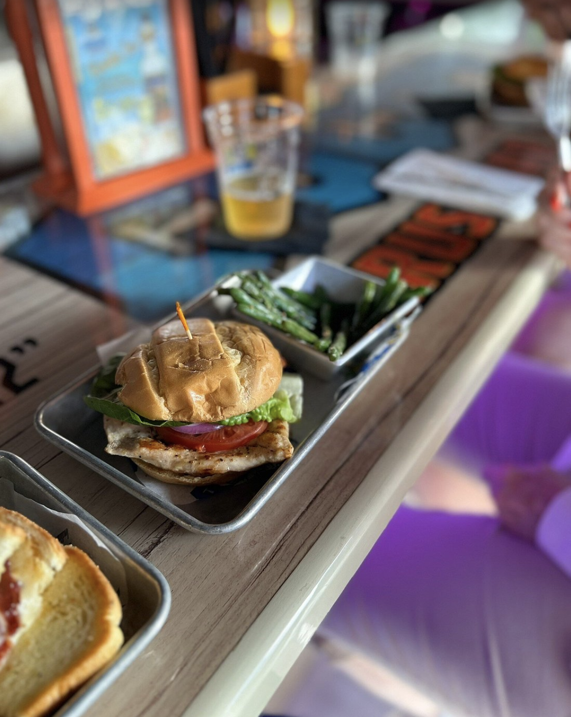 Grilled chicken sandwich with lettuce, tomato, and onion served with green beans.