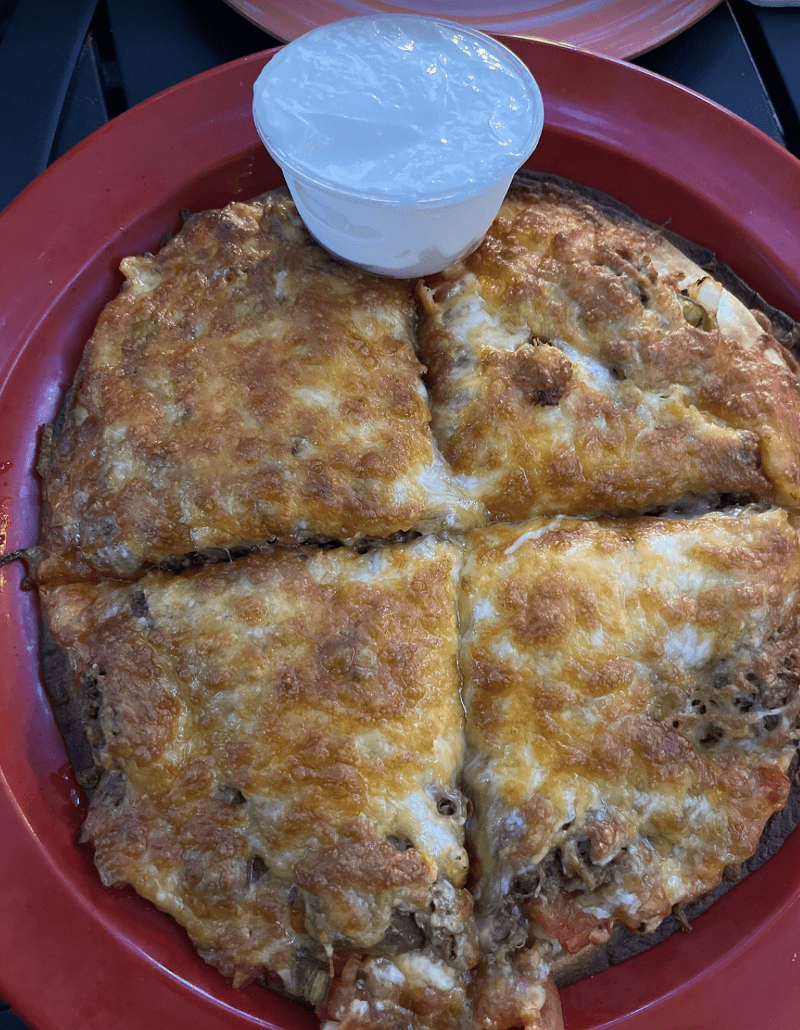 Cheesy pizza served with a cup of ranch dressing on a red plate.