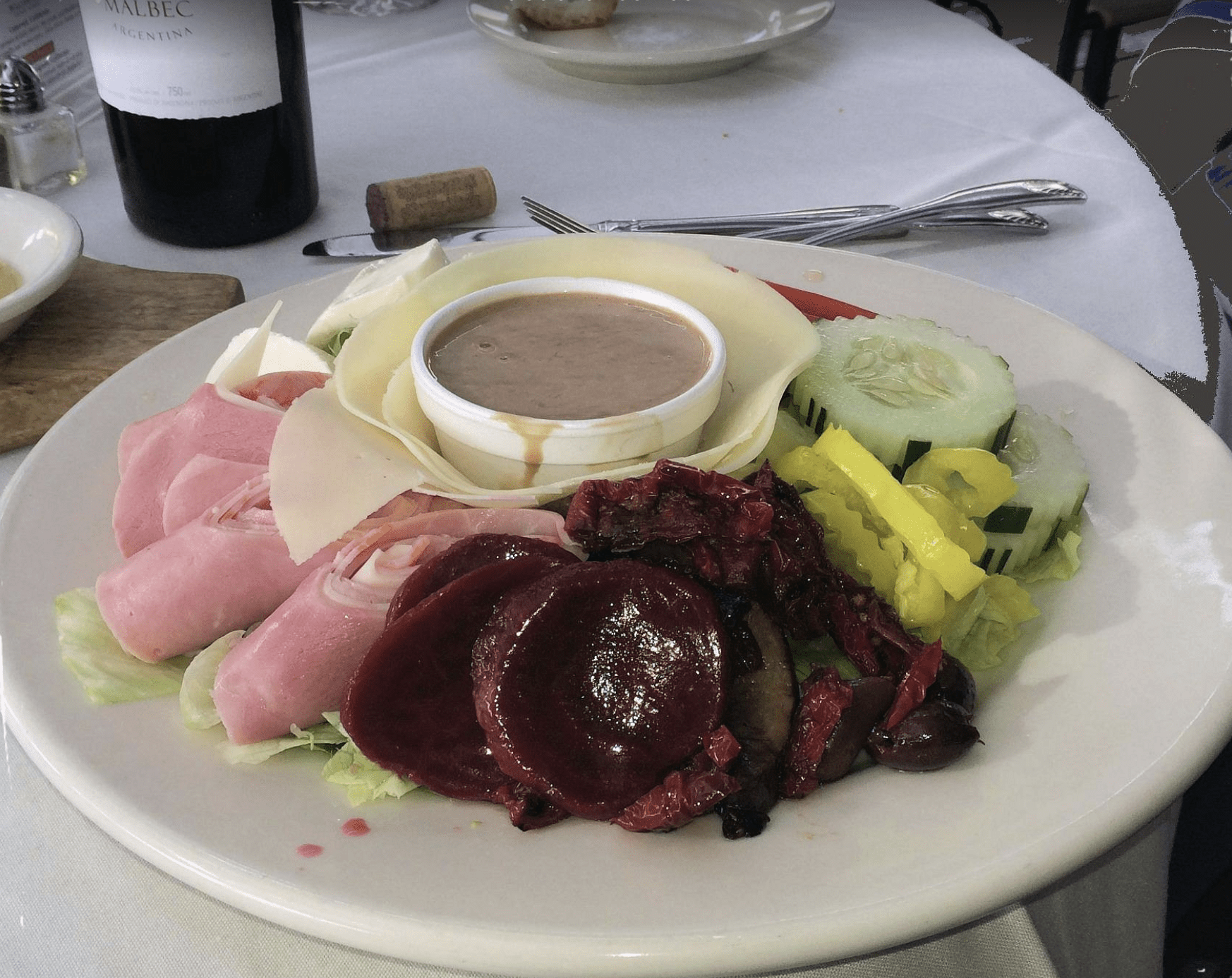 Seafood and cold-cut salad plate with ham rolls, cheese slices, vegetables, and dressing.