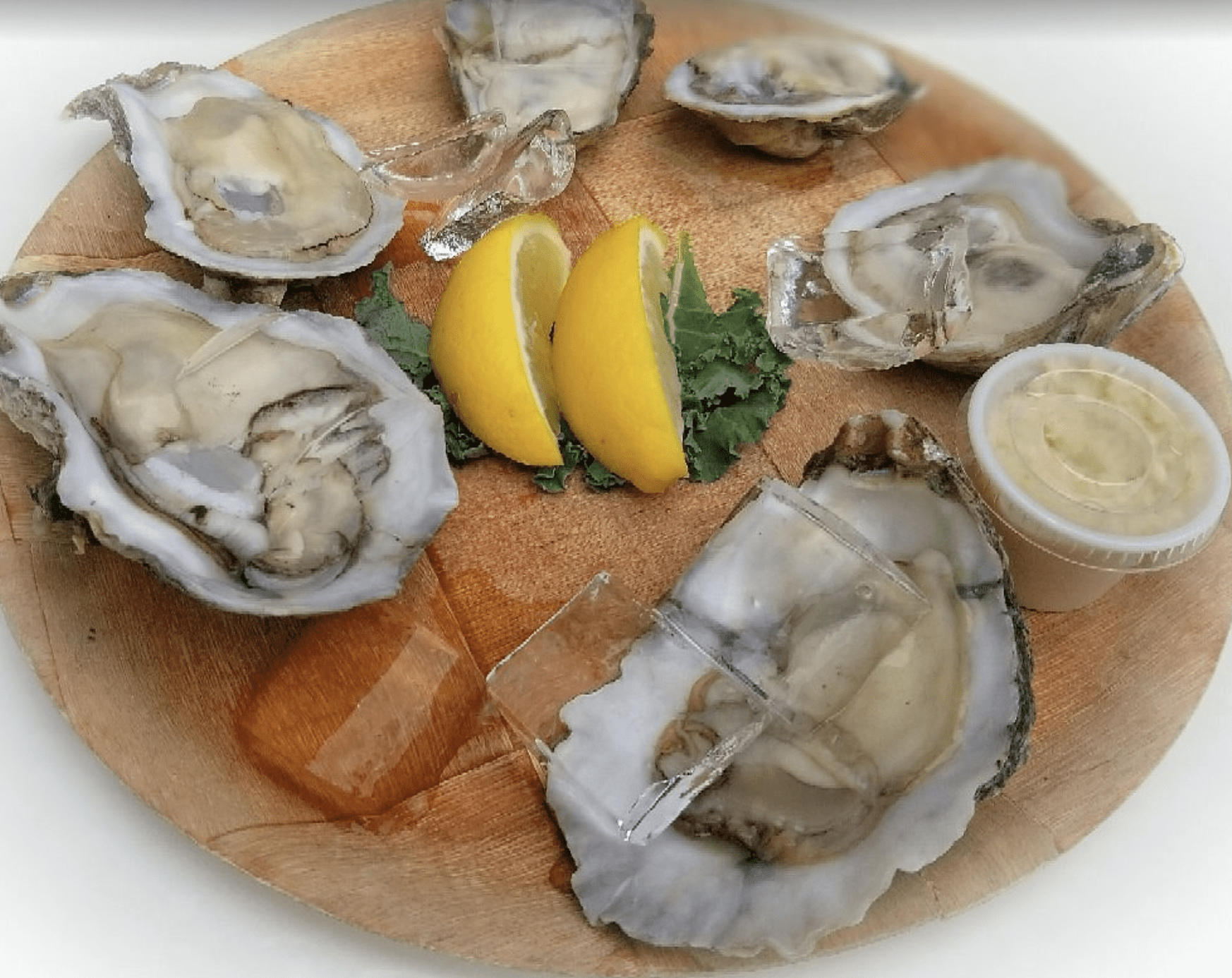 Fresh oysters on ice with lemon wedges and dipping sauce on a wooden serving board.