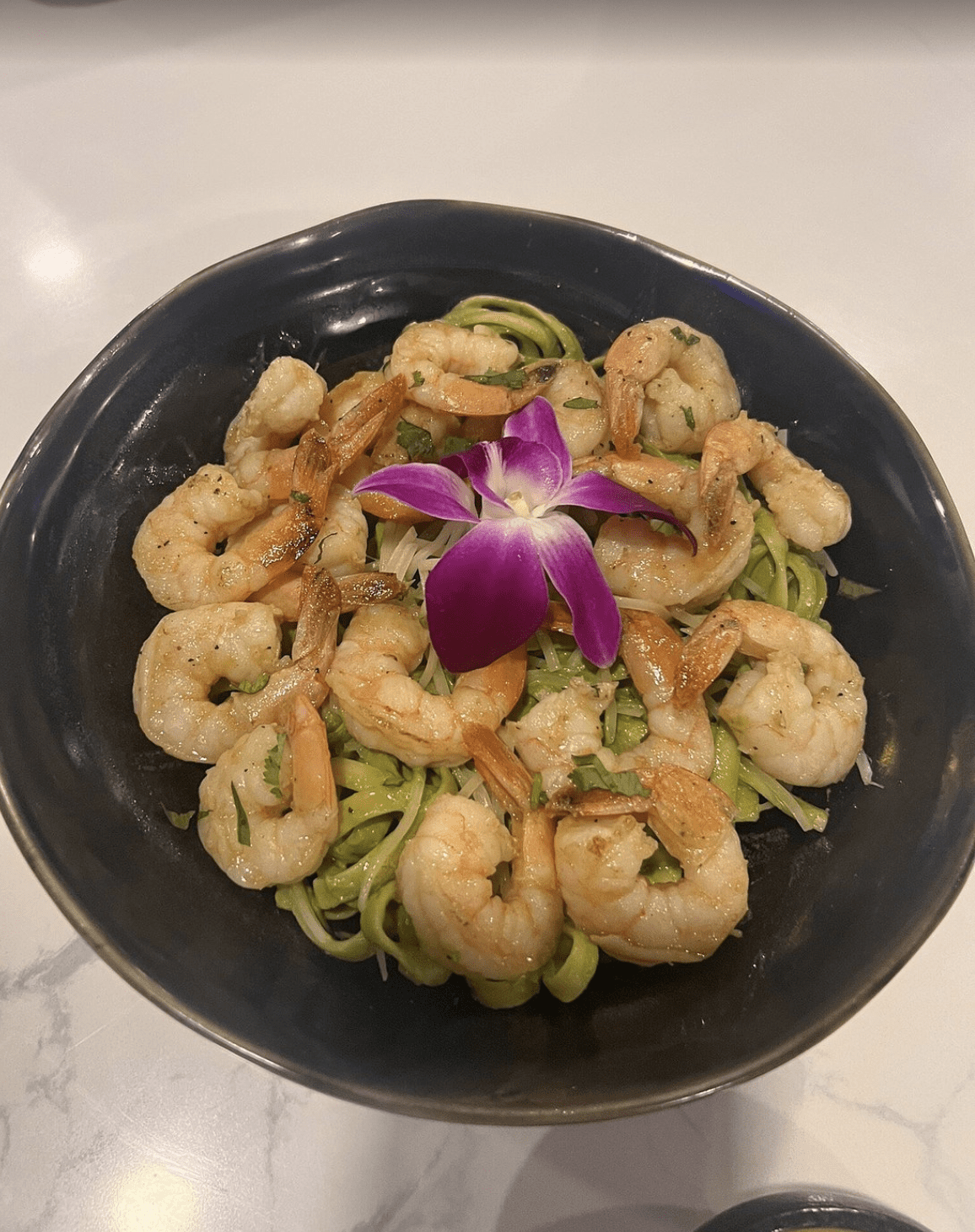 Garlic shrimp served over green pasta with a purple edible orchid at a Clearwater Beach restaurant.