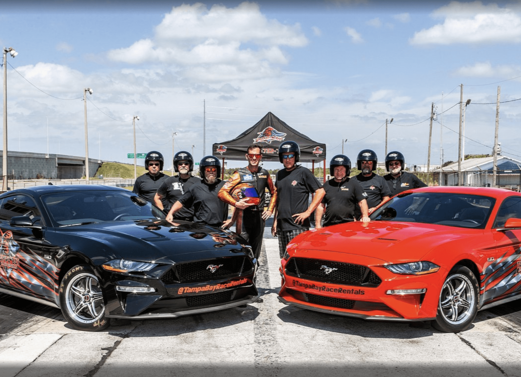 Group of drivers posing with race cars at Tampa Bay Race Rentals track.